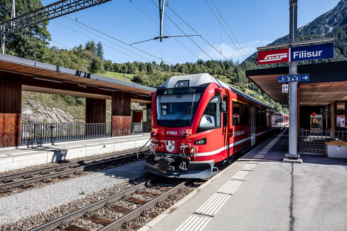 Roter Zug der Rhätischen Bahn steht am Bahnsteig des Bahnhofs Filisur vor alpiner Kulisse