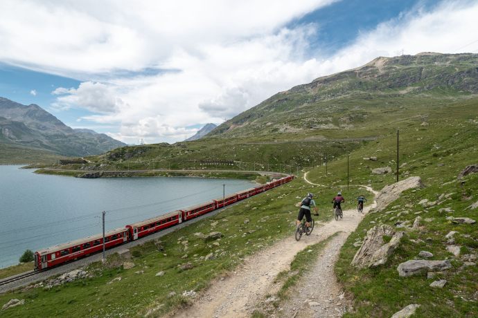 Mountainbiker auf Trail am Lago Bianco mit Blick auf die Rhätische Bahn