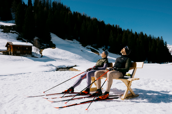 Patgific Pause machen und die Sonne geniessen (Foto: © GRF, Filip Zuan) Zwei Langlaufende auf einer Bank sich am sonnen