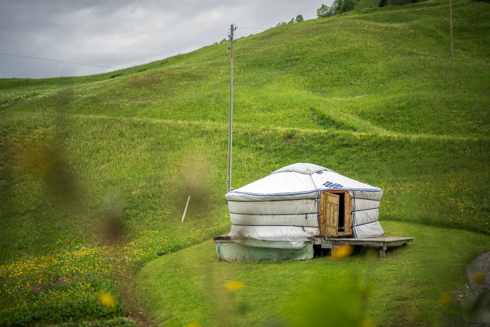 Runde Jurte mit Holztür auf einer Wiese inmitten grüner Hügel.