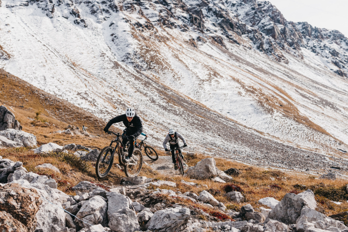 wei Mountainbiker fahren auf einem steinigen Trail durch hochalpines Gelände.