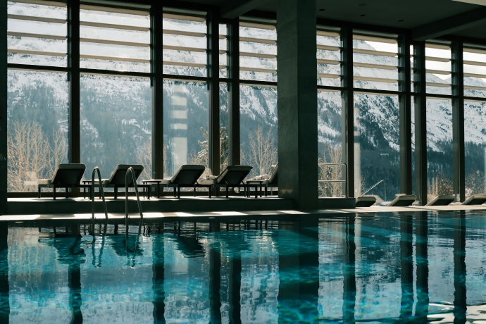Piscine intérieure du Kulm Hotel St. Moritz avec une ambiance spa élégante (Photo : © Kulm Hotel St. Moritz) Piscine intérieure avec chaises longues et vue panoramique sur les montagnes environnantes depuis le Kulm Hotel St. Moritz