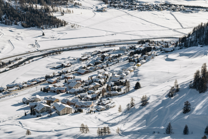 Find peace in the smallest village of the Upper Engadin – and then glide with renewed energy along the ice trail from Madulain to nearby Zuoz (Photo: © Engadin Tourismus AG) Aerial view of Madulain in the Upper Engadin, surrounded by snow-covered meadows and mountains