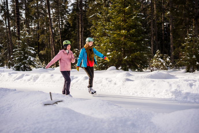 When the ice sparkles in the winter sun, the natural ice trail reveals its most beautiful side (Photo: © Dominik Täuber / Tourismus Engadin Scuol Samnaun Val Müstair AG) Two women ice skating on the Ice Trail Engadin in the winter forest