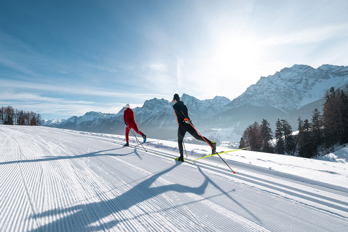 Zwei klassische Langläufer im Unterengadin (Foto: © Filip Zuan) Zwei Langläufer in sportlicher Ausrüstung gleiten durch eine perfekt präparierte Loipe im Unterengadin, umgeben von verschneiten Bergen und einer klaren Winterlandschaft bei strahlendem Sonnenschein.