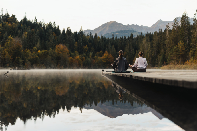 Zwei Frauen machen Yoga an einem Bergsee.