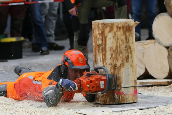 Ein Holzfäller sägt liegend mit einer Motorsäge einen Baumstamm bei einem Wettbewerb in Lostallo