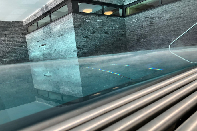 Entspannung mit Stil: Der moderne Wellnessbereich im Catrina Resort in Disentis bietet Erholung im warmen Wasser mit Blick auf die Bündner Bergwelt (Foto: © CATRINA EXPERIENCE) Schwimmbad mit Steinwänden und warmem Licht im Wellnessbereich des Catrina Resort in Disentis