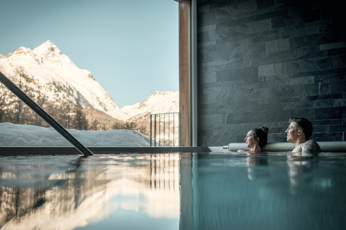 Wellness mit Weitblick: Der Spa-Bereich des Nira Alpina in Silvaplana lädt ein zum Abschalten mit direktem Blick auf die Engadiner Bergwelt (Foto: © Schweiz Tourismus / Lorenz Richard) Paar entspannt im Indoor-Pool mit Blick auf schneebedeckte Berge im Wellnessbereich des Nira Alpina