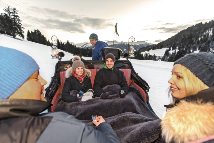 Eine Gruppe fährt in einer Kutsche eingehüllt in Decken durch die verschneite Landschaft