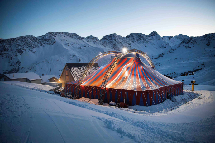Beleuchtetes Festzelt des Arosa Humorfestivals inmitten verschneiter Berglandschaft bei Abenddämmerung