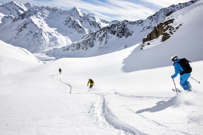 Trois skieurs tracent des lignes fraîches dans la neige poudreuse en descendant un large versant