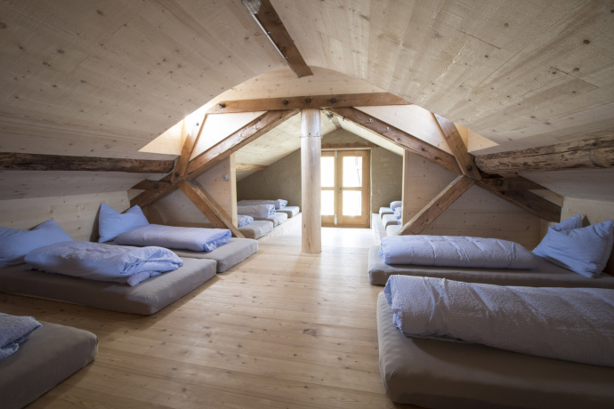 Schlafraum der Gruppenunterkunft Alp Nurdagn im Agrotourismusbetrieb, mit mehreren Matratzenlagern unter dem Dach und hellen Holzelementen
