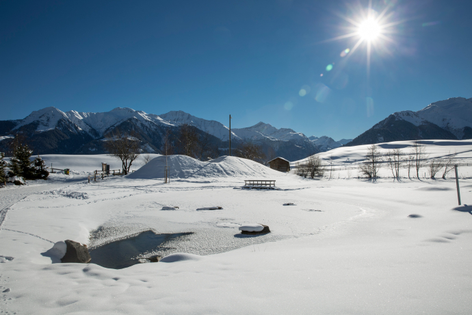 Der Badesee Davos Munts in der Lumnezia ist bedeckt mit Schnee bei bestem Winterwetter. Neu kann man hier auch ein Eisbad nehmen.