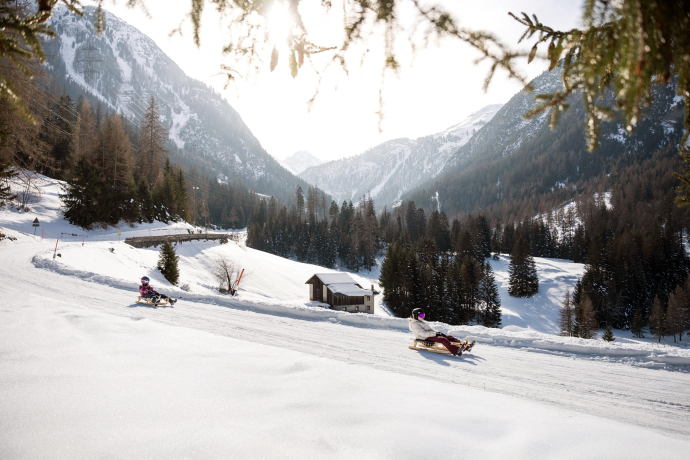Zwei Personen schlitteln in wunderschöner Winterlandschaft in Preda-Bergün die Schlittelpiste hinunter.
