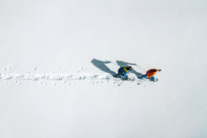 Zwei Schneeschuhwanderer aus der Luft auf schmaler Spur durch unberührten Schnee mit langen Schatten