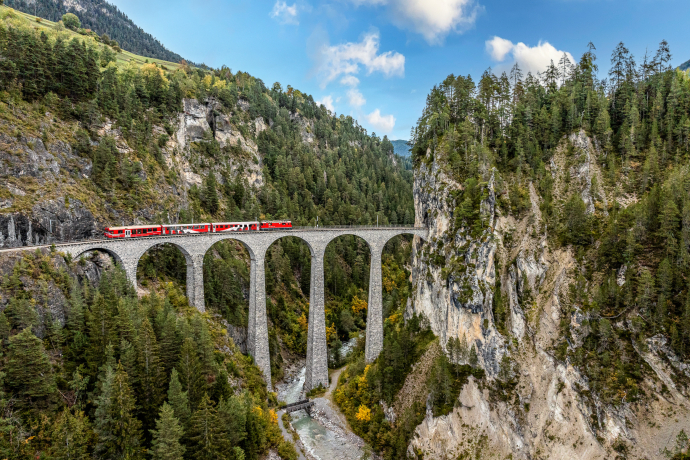 Ein offener Aussichtswagen der Rhätischen Bahn fährt über das Landwasserviadukt in Richtung des Tunnelportals