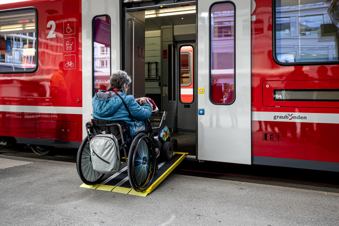 Person im Rollstuhl fährt über eine Rampe in einen Zug der Rhätischen Bahn