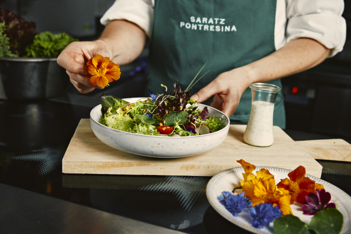Ein Koch dekoriert einen frischen Salat mit essbaren Blüten aus dem eigenen Garten