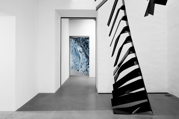 Moderner Museumsinnenraum mit einer schwarzen, skulpturalen Treppe und dem Blick in eine Felsengrotte