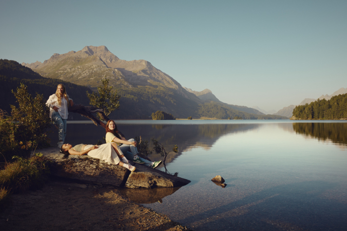 Drei junge Frauen entspannen auf einem Baumstamm am Ufer des Silsersees