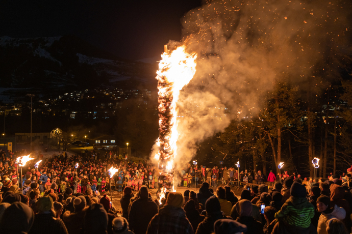 Une grande foule regarde un immense bonhomme de paille en feu la nuit