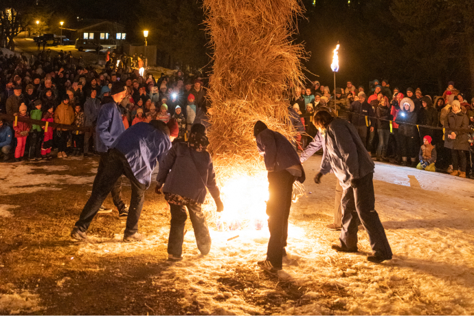 Plusieurs personnes allument un grand bonhomme de paille la nuit devant une foule