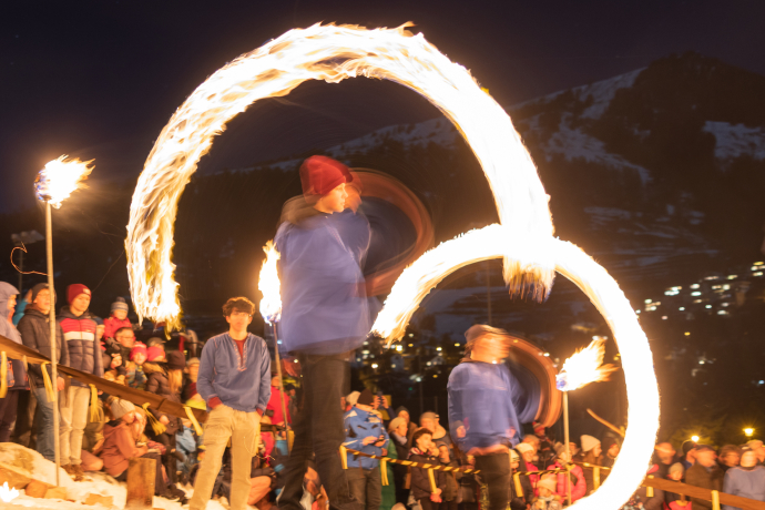 Une personne fait tournoyer deux grands cercles de feu la nuit devant un public