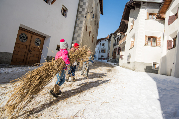 Des enfants portent des bottes de paille en montant une ruelle enneigée