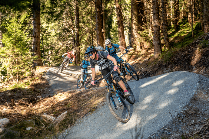 Familie ist gemeinsam auf dem Foppa Trail in Flims unterwegs, umgeben von einer grünen Waldlandschaft.
