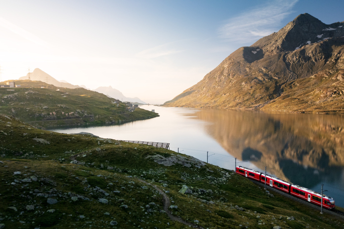 Rhätische Bahn fährt am Lago Bianco vorbei, umgeben von Alpenbergen und grünen Wiesen in Valposchiavo.