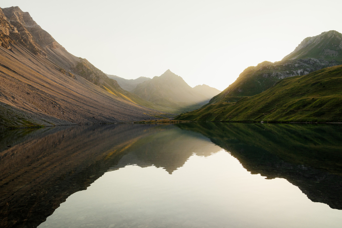 Alpilisee in Arosa Lenzerheide mit spiegelglatter Wasseroberfläche, umgeben von grünen Hängen und schroffen Bergspitzen.
