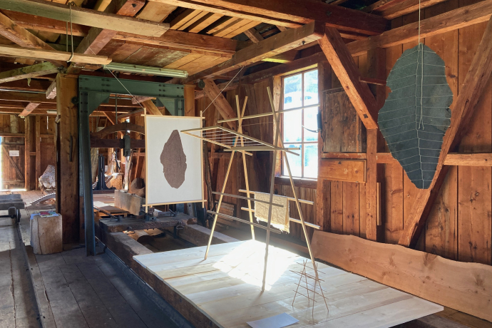 Holzausstellung mit filigranen Holzkonstruktionen und hängenden Kunstobjekten in einer historischen Sägerei aus dunklem Holz