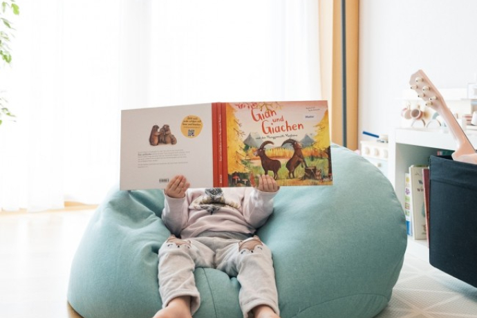 Sitzendes Kind liest das Buch "Gian und Giachen und das Munggamaitli Madlaina"