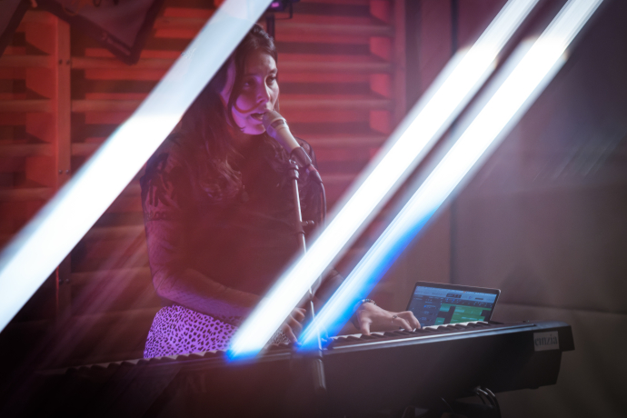 Musikerin singt an einem Mikrofon und spielt Keyboard bei stimmungsvoller Bühnenbeleuchtung