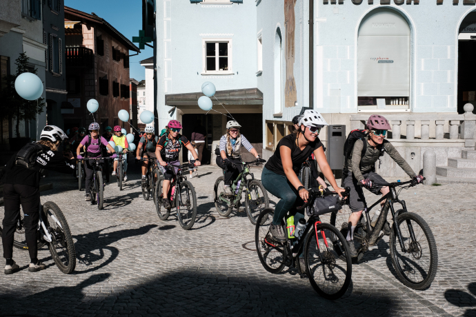 Zahlreiche Velofahrerinnen mit hellblauen Luftballons an den Velos fahren über den gepflasterten Dorfplatz von Samedan