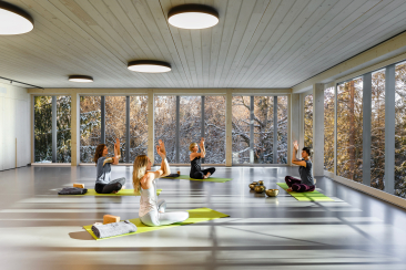 Vier Frauen sitzen im Schneidersitz auf grünen Yogamatten im Badehaus des Romantik Hotel Schweizerhof Flims