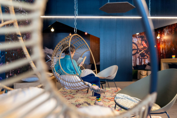 Eine junge Frau sitzt entspannt in einem Korbstuhl in der Lobby des Hotel Aves in Arosa und liest ein Buch