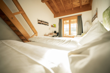 Ein Doppelbett mit weisser Bettwäsche in einem Zimmer im Hotel Ucliva in Waltensburg
