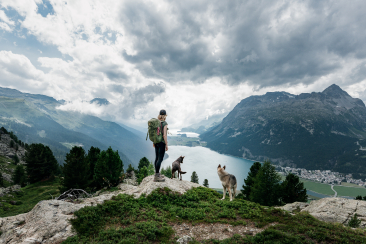 Eine Wanderin geniesst mit ihren beiden Hunden die Aussicht auf die Oberengadiner Seenplatte