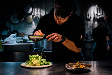Ein Koch reibt Zitronenschale über einen Salat in der Küche des Riders Restaurant in Laax