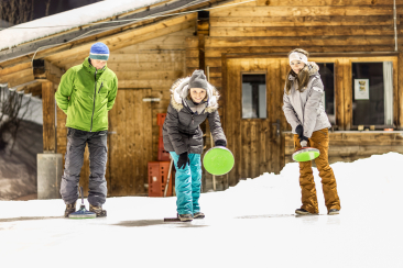 Eine Frau schwingt ihren Eisstock auf dem Natureisplatz Samnaun Clis da Ravaisch