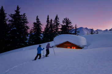 Ein Paar in Schneeschuhen stapft zu einer Berghütte