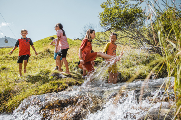 Kinder spielen an einem kleinen Bachlauf auf einer Wiese in Arosa