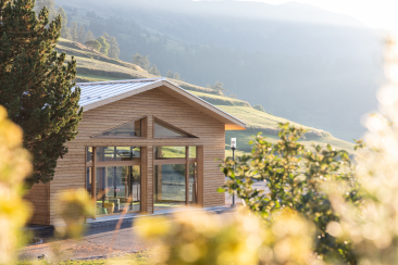 Das Yoga-Haus, ein Holzbau mit grossen Panoramafenstern und Giebeldach, auf einer grünen Bergwiese im Meisser Resort in Guarda