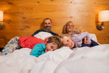 Eine Familie mit zwei kleinen Kinder liegt auf einem Bett eines Apartments im rocksresort LAAX