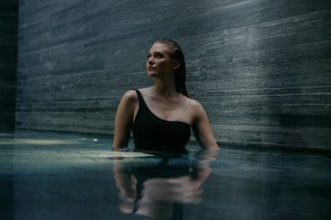 Eine junge Frau in einem schwarzen Badeanzug steht in einem Innenbad der 7132 Therme in Vals