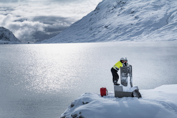 Ein Mann bei Vermessungsarbeiten an einem zugefrorenen Stausee in winterlicher Landschaft in Graubünden