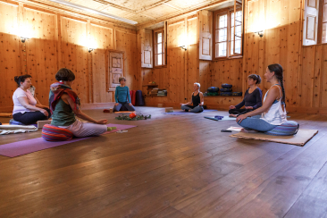 Eine Gruppe von Personen praktiziert Yoga in einem lichtdurchfluteten Raum des Alten Klosters in Poschiavo