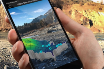 Hand hält Smartphone mit Augmented-Reality-App zur Besucherlenkung in alpiner Landschaft